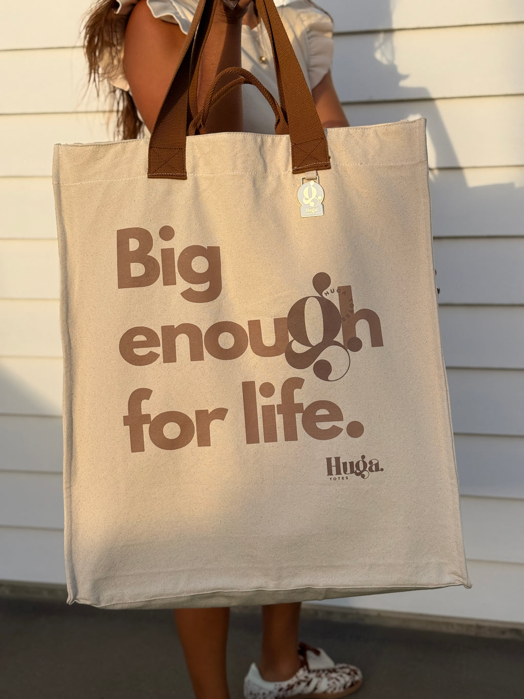 Person holding a beige tote bag with 'Big enough for life' text and Huga logo.